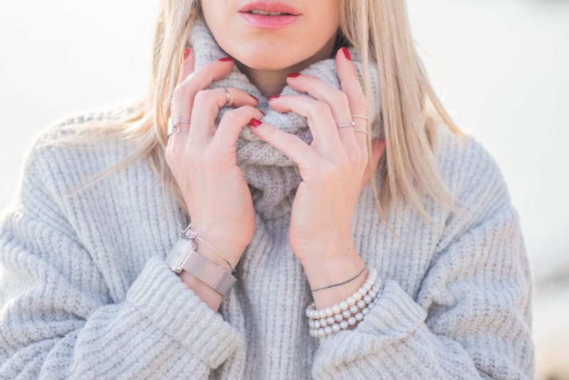 Frau hält den Kragen eines grauen Strickpullovers