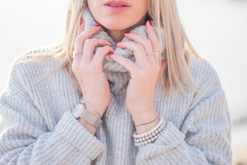 Frau hält den Kragen eines grauen Strickpullovers