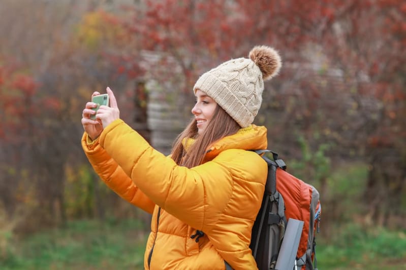 Woman in a mustard puffer taking a photo with her phone