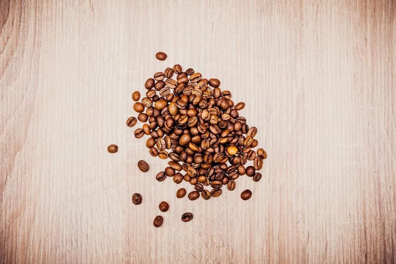 Small heap of coffee beans on light wood