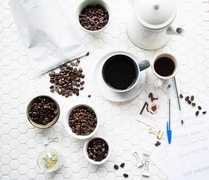 Kaffeeflatlay mit Bohnen, Tassen und Kanne auf Weiß