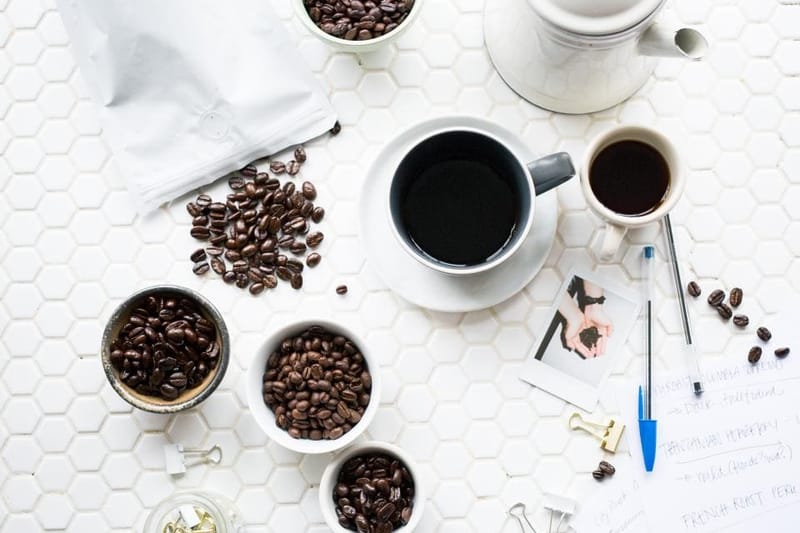 Kaffeeflatlay mit Bohnen, Tassen und Kanne auf Weiß
