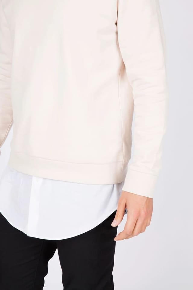 Model in ecrufarbenem Sweatshirt vor weißem Hintergrund
