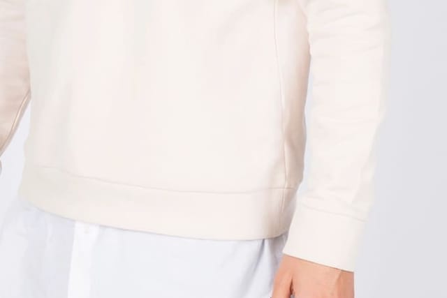 Model in ecrufarbenem Sweatshirt vor weißem Hintergrund