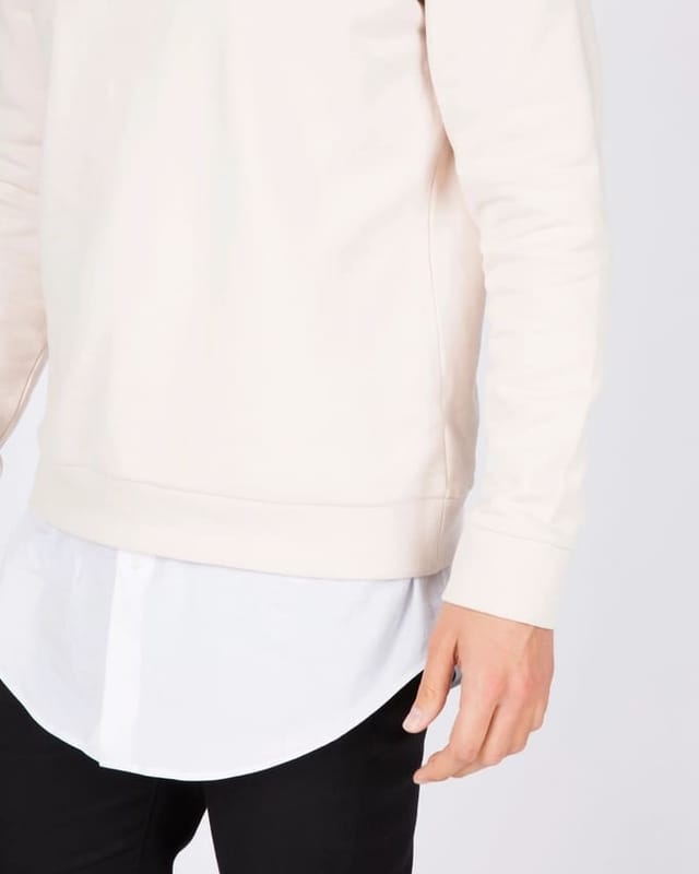 Model in ecrufarbenem Sweatshirt vor weißem Hintergrund