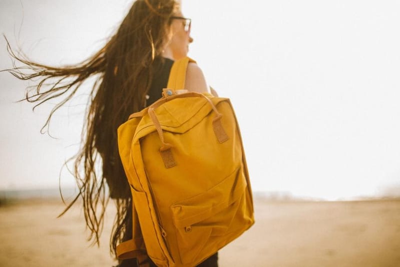 Frau mit senfgelbem Rucksack im Wind