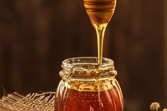 Honig tropft vom Honiglöffel in ein Glas