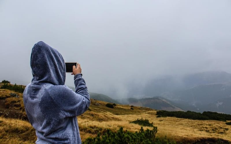 Person in blauem Hoodie fotografiert Hügellandschaft