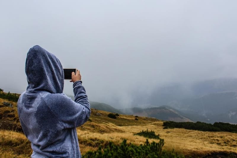 Person in blauem Hoodie fotografiert Hügellandschaft