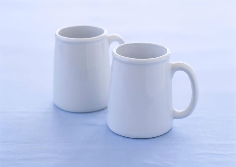 Zwei weiße Becher vor hellblauem Hintergrund