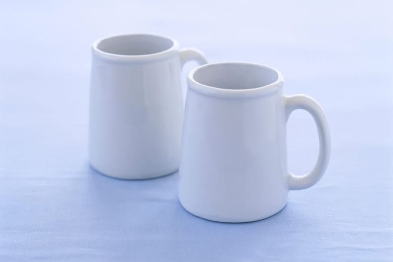 Zwei weiße Becher vor hellblauem Hintergrund