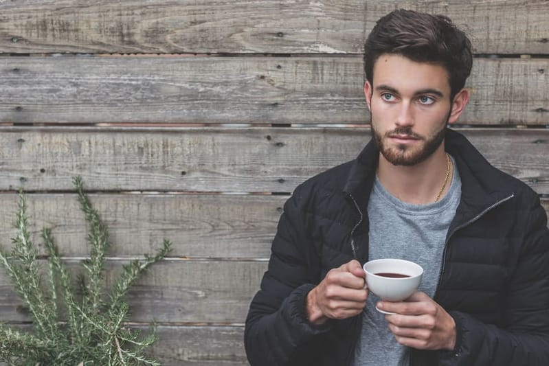 Man in a black quilted jacket holding a coffee cup