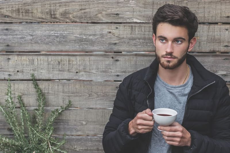 Man in a black quilted jacket holding a coffee cup