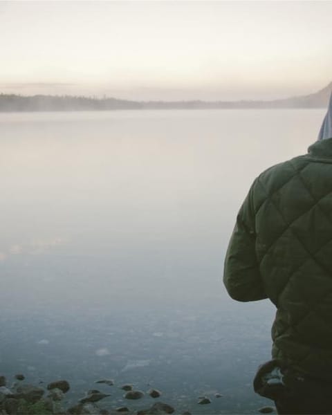 Person in an olive quilted jacket by a lake