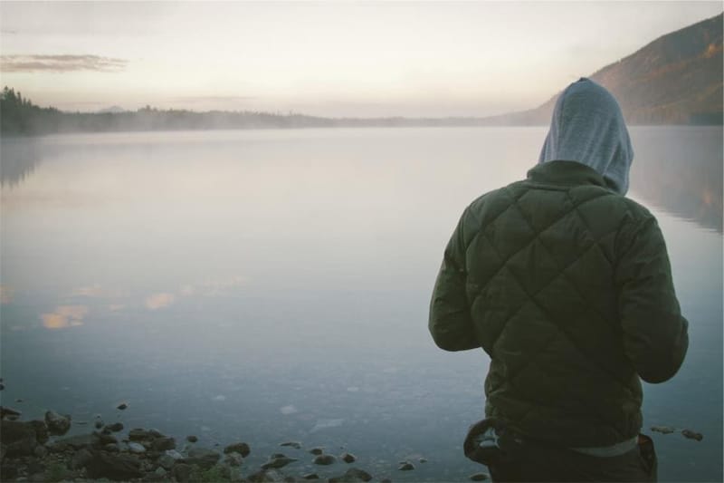 Person in an olive quilted jacket by a lake