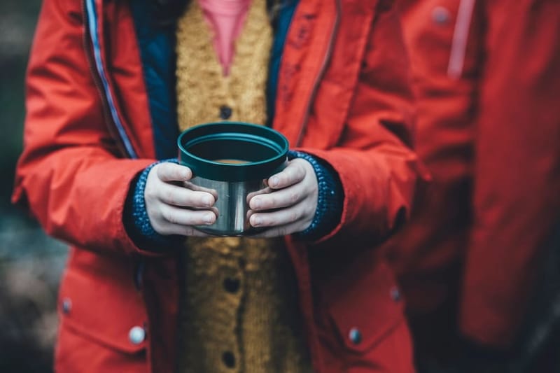 Hands in a red jacket holding an enamel cup