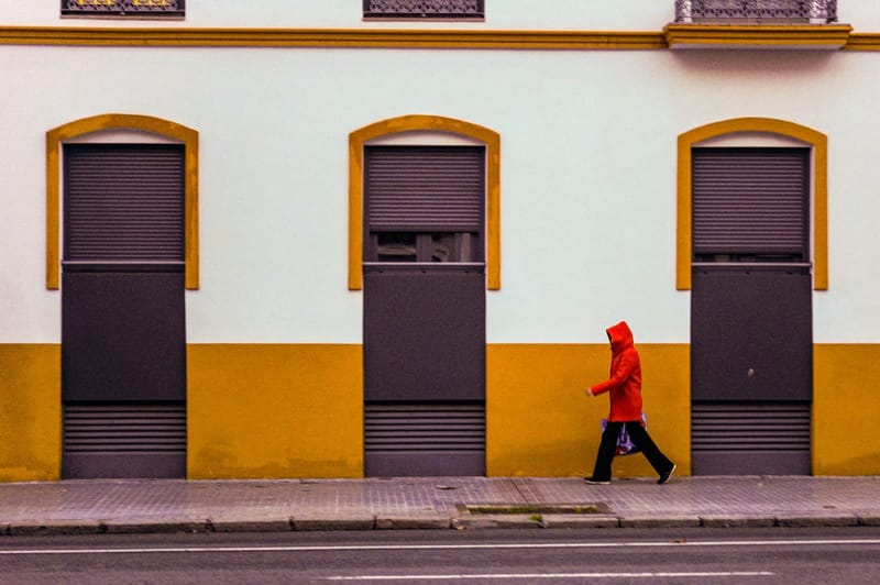 Person in a red rain jacket in front of a yellow facade