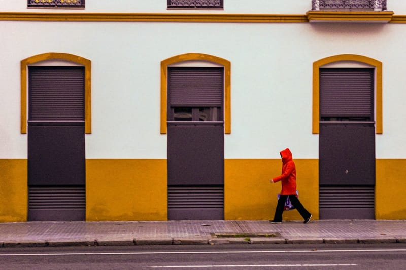 Person in a red rain jacket in front of a yellow facade