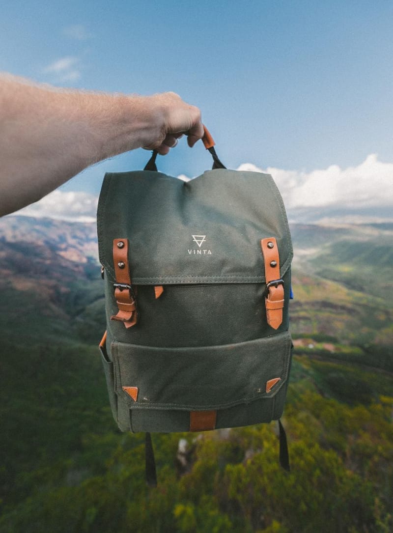 Olivgrüner Canvas-Rucksack mit Lederriemen vor Landschaft