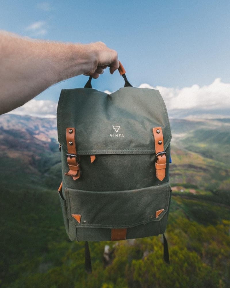 Olivgrüner Canvas-Rucksack mit Lederriemen vor Landschaft
