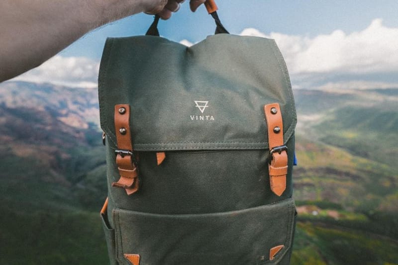 Olivgrüner Canvas-Rucksack mit Lederriemen vor Landschaft