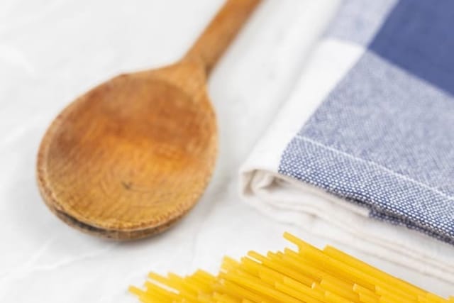 Blau kariertes Geschirrtuch mit Holzlöffel und Nudeln