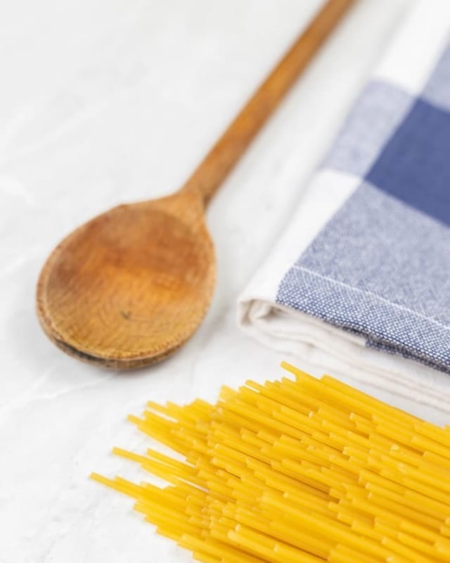 Blue check tea towel with a wooden spoon and pasta