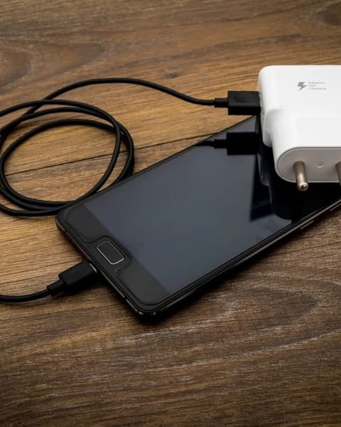 Weißes Netzteil mit EU-Stecker lädt ein Smartphone auf Holz