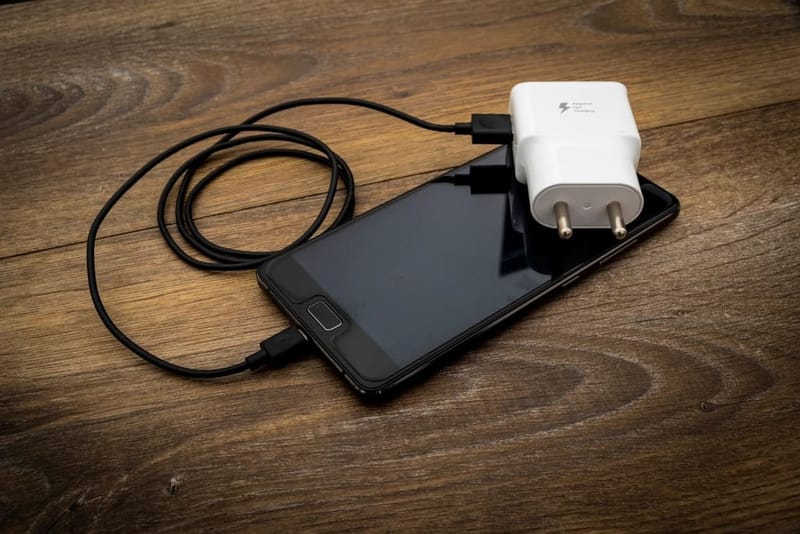 Weißes Netzteil mit EU-Stecker lädt ein Smartphone auf Holz