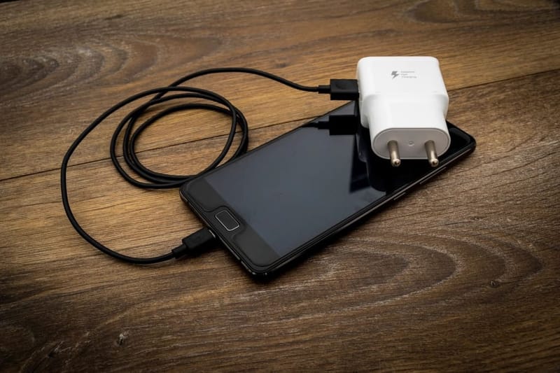 Weißes Netzteil mit EU-Stecker lädt ein Smartphone auf Holz