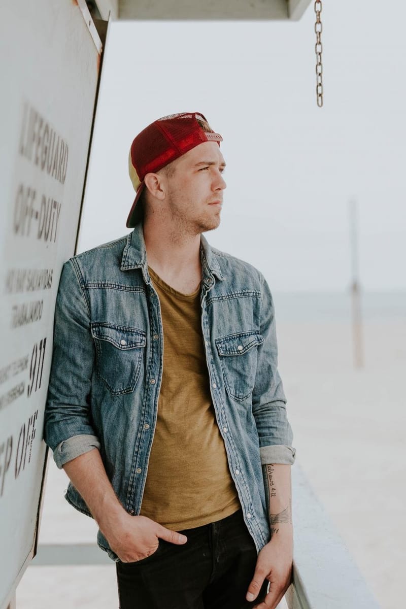 Man in a cap wearing a denim jacket on the coast