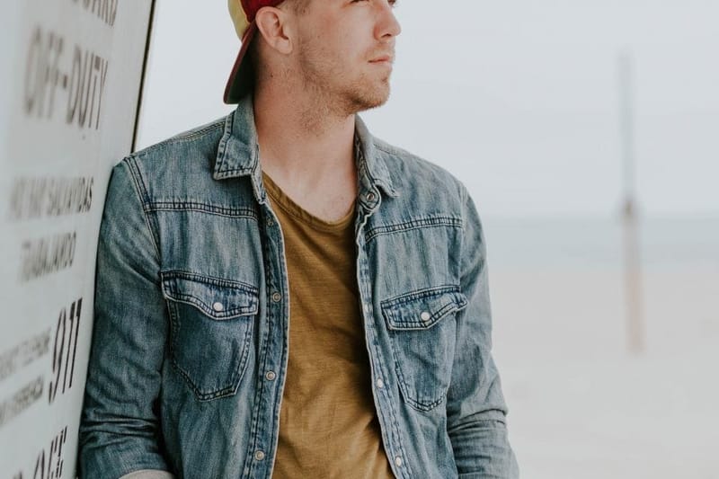 Man in a cap wearing a denim jacket on the coast